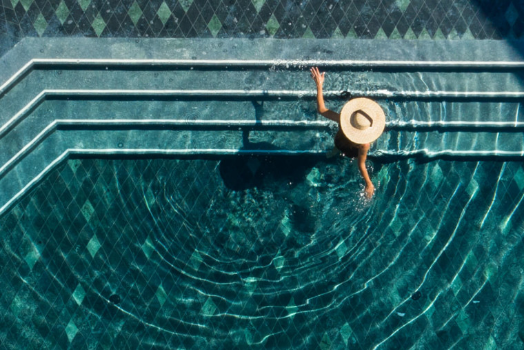 Person mit Hut entspannt im Pool, Blick von oben auf Wasserbewegungen