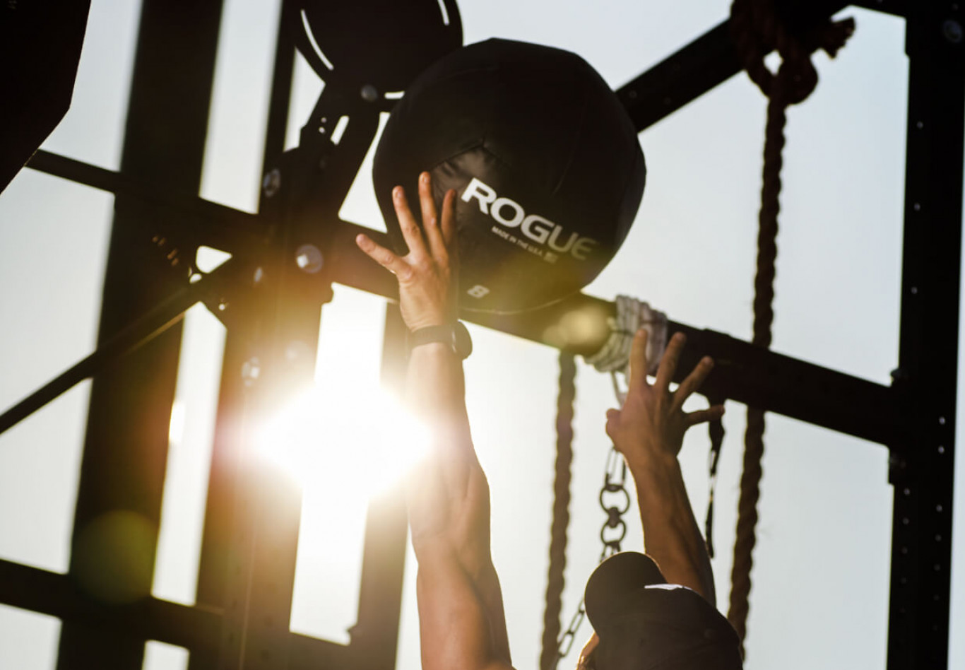 Sportler wirft einen Medizinball an einem Outdoor-Trainingsgerüst bei Sonnenlicht