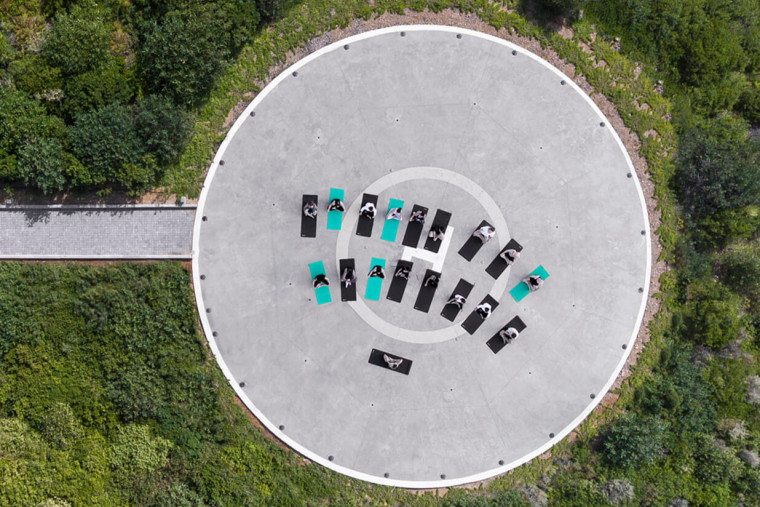Gruppe von Menschen auf Yogamatten in kreisförmiger Outdoor-Anlage, Luftaufnahme