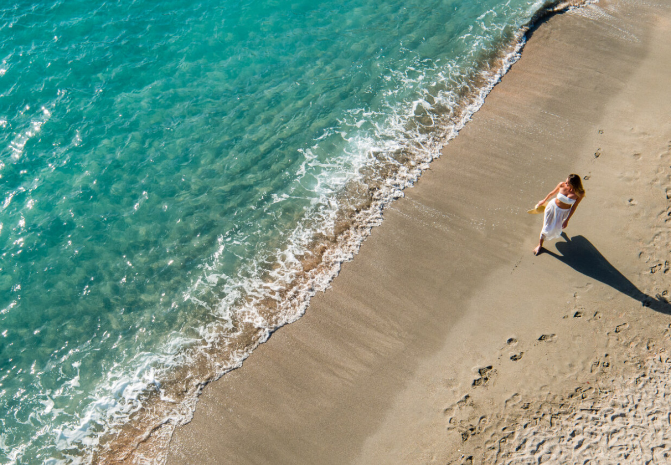Luftaufnahme einer Frau am Strand mit Wellen, die ans Ufer rollen